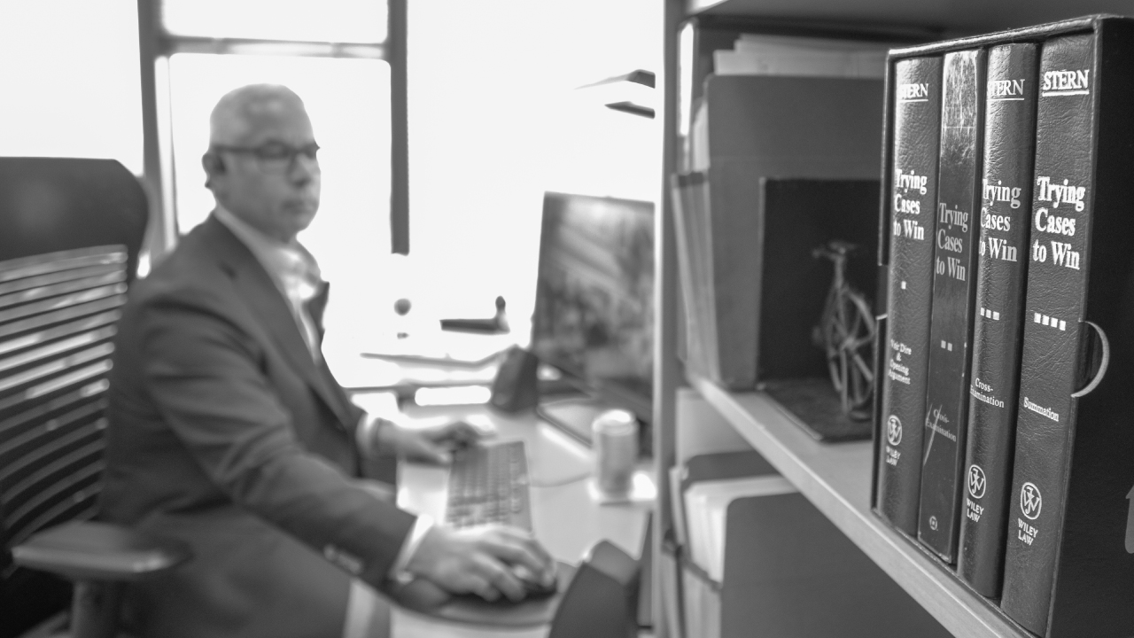 A Patterson Thuente IP Litigation Lawyer works on a case in his office. A set of books titled "Trying Cases to Win" by Wiley Law can be seen in the foreground.